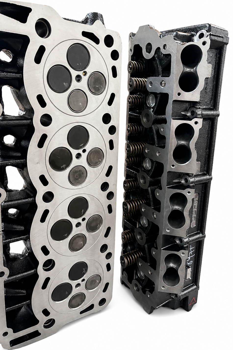 Two engine cylinder heads photographed on a white background, one showing the silver headland and valve seat area, and the other showing the dark cast iron side with springs and ports.