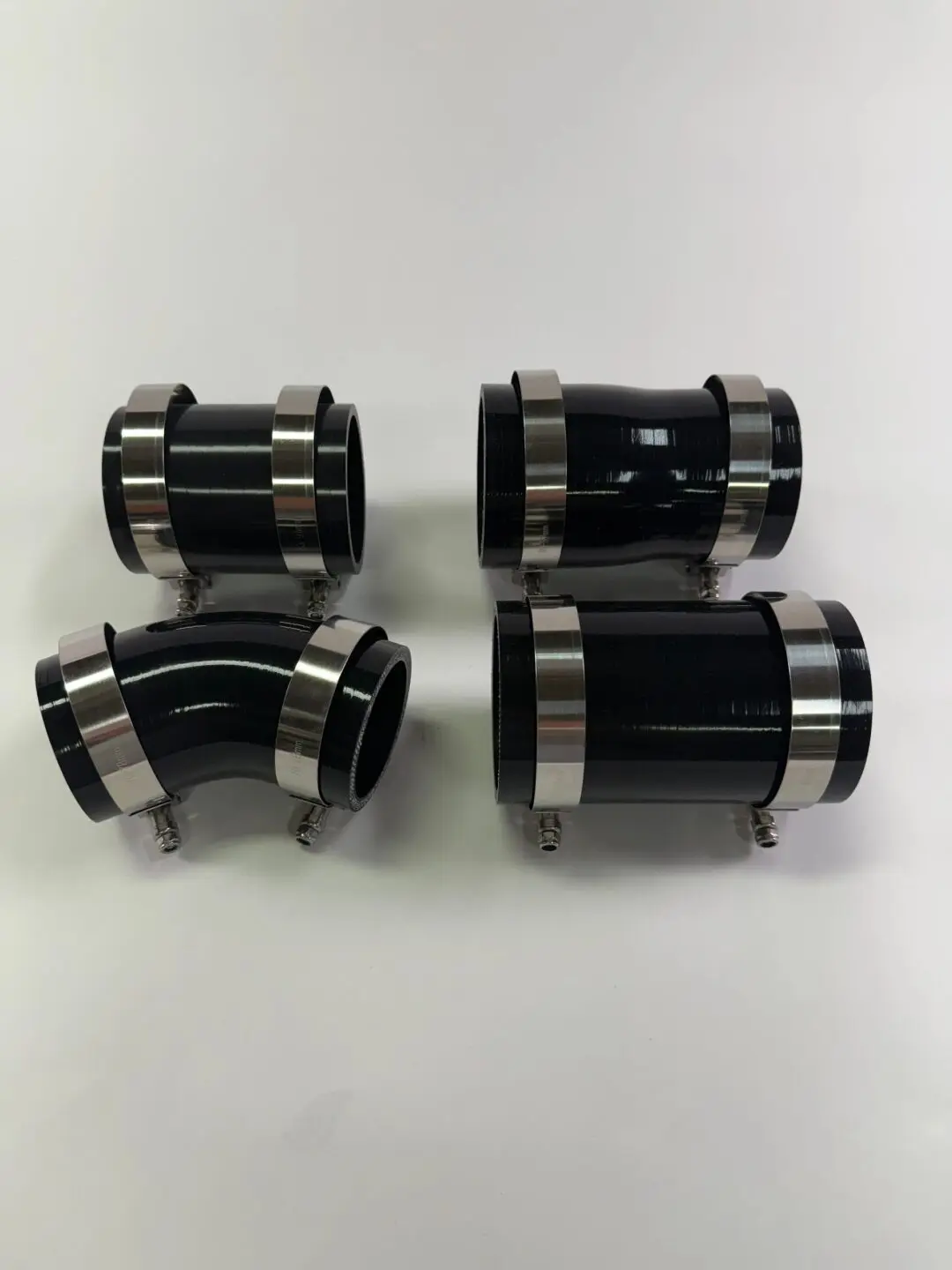 Four black and silver mechanical couplings or connectors.